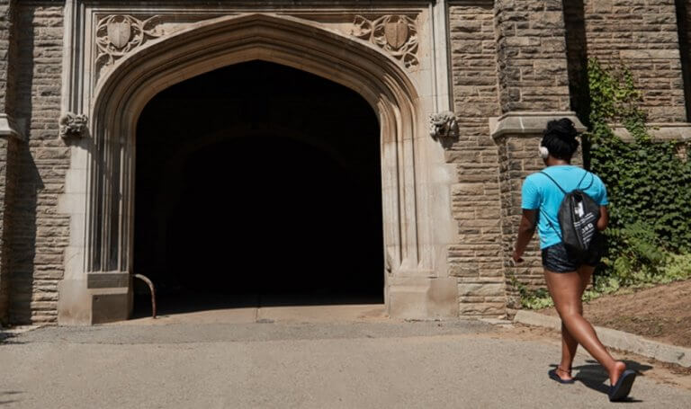 Student walking through University Hall arch in summer.