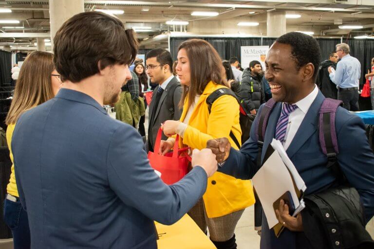 Students bumping fists, dressed in professional attire at Connect to Careers Job Fair.