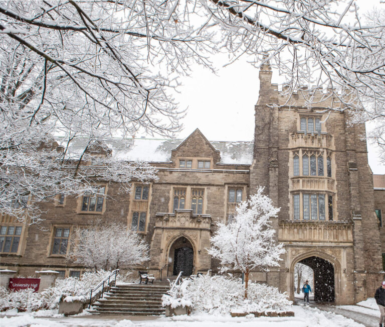 Campus grounds during snowfall. View of University Hall.