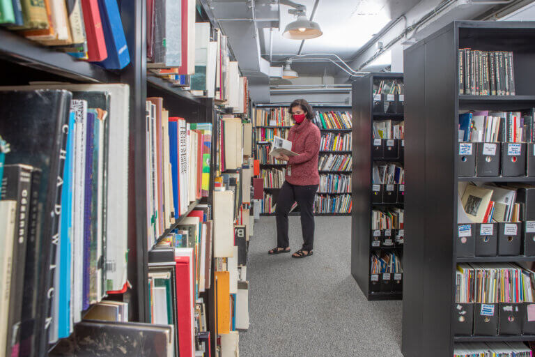 Library employee standing in row of book at Art Education Library.