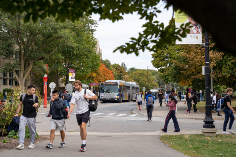Groups of students walking around busy campus by the bus stop.
