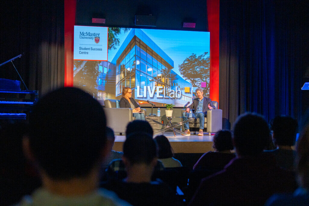 Roma and Rob sitting on stage. Audience is visible. 