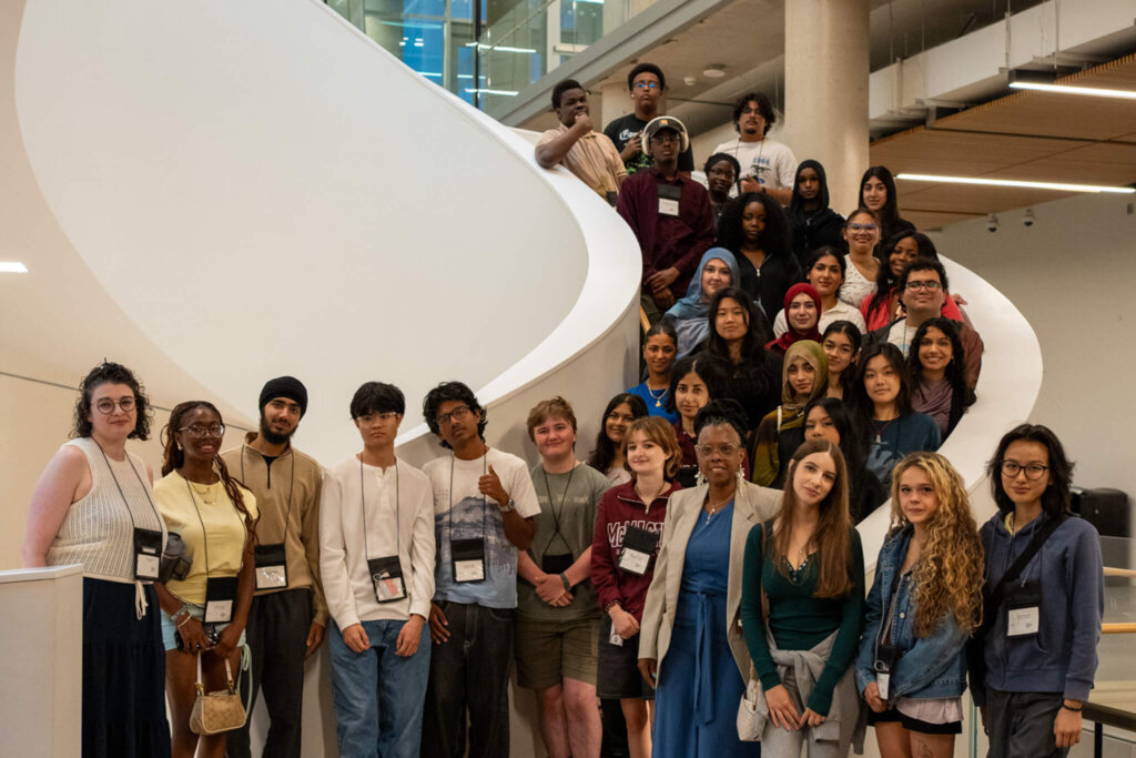Large, diverse group of students and adults pose cheerfully on a sweeping indoor staircase in a bright, modern atrium.