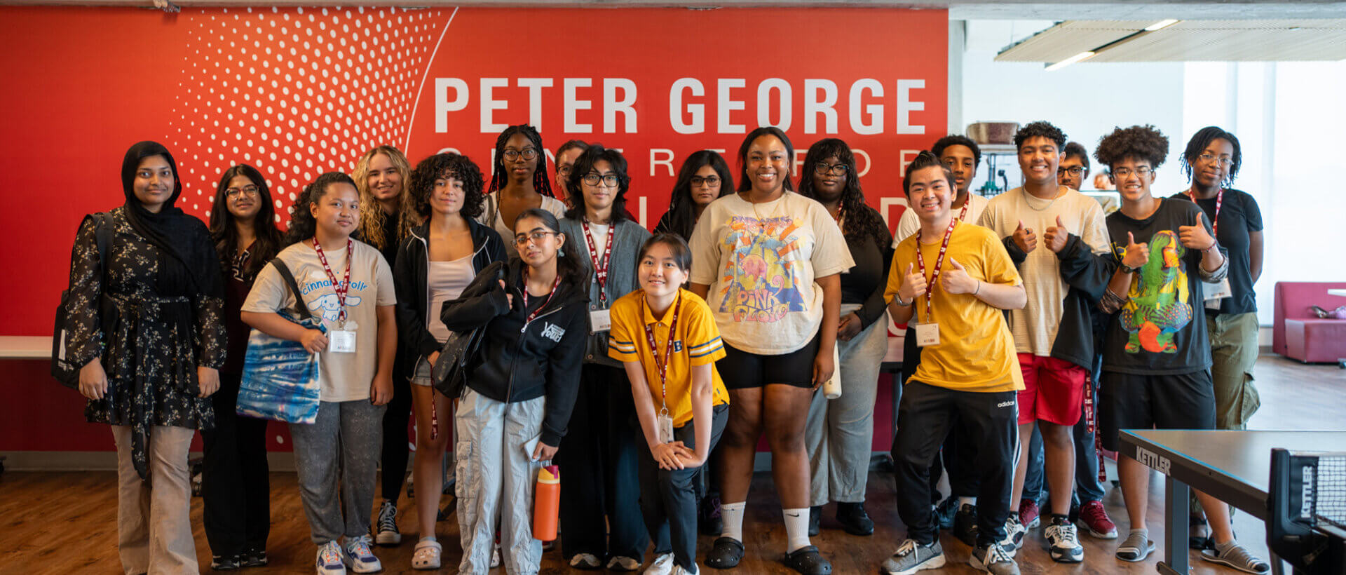 A diverse group of students stands smiling in front of a wall with