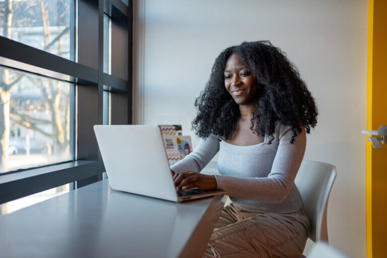 Student working on laptop by a window.